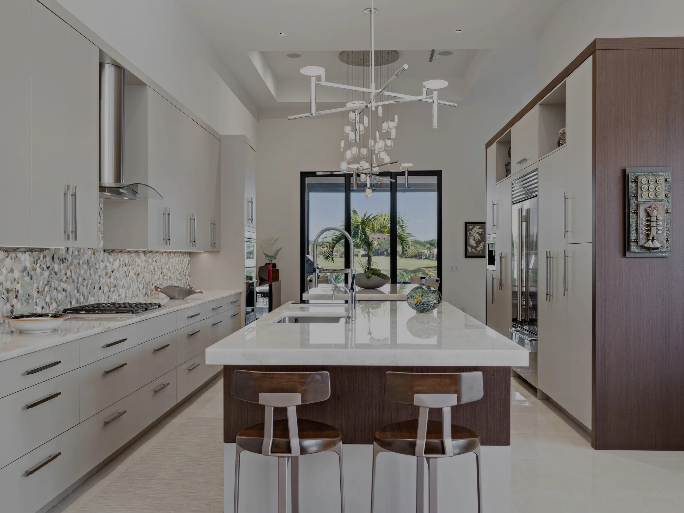 Custom kitchen with pale flat-panel cabinetry, a walnut-clad island under a marble counter and a pebble mosaic backsplash, Palm Beach County residence, Jupiter FL